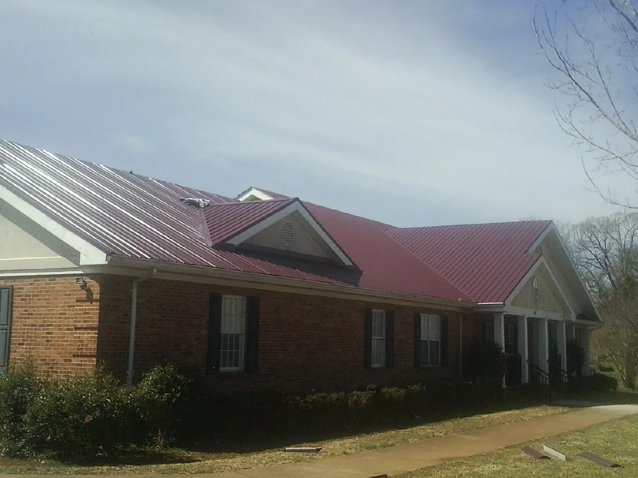 Red metal roof with gabled entries on a long brick building, from a Hail Damage Roof Repair job in Cullowhee