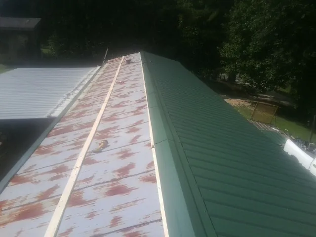 Old rusted panels beside newly installed green metal roofing — Wind Damage Roof Repair by Roofing Brothers in Cullowhee