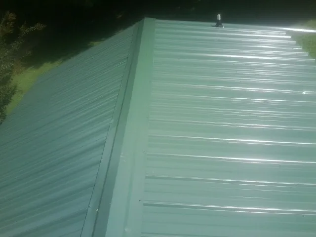 New green metal panels meeting at the ridge of a roof — Flat Roof Repair work by our crew in Cullowhee
