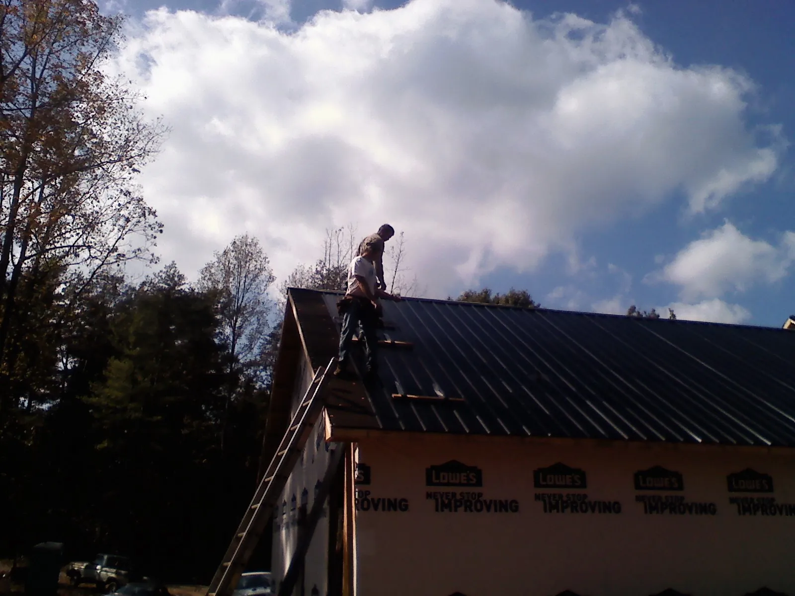 Roofer fastening dark metal panels high against a cloudy sky, from a Roof Inspection job in Cullowhee