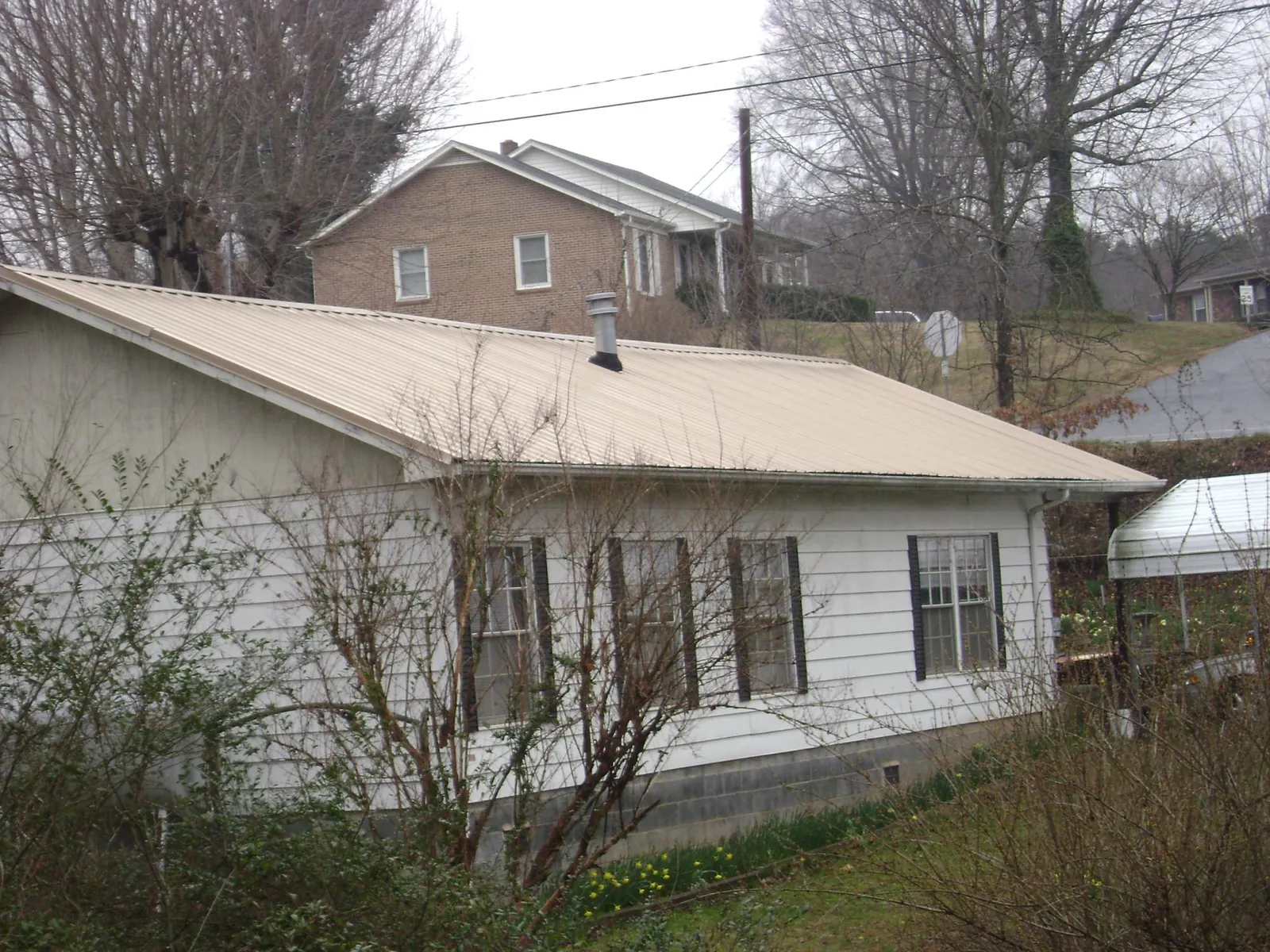 Tan metal roof on a white sided house set into a hillside — Commercial Roofing by Roofing Brothers in Cullowhee
