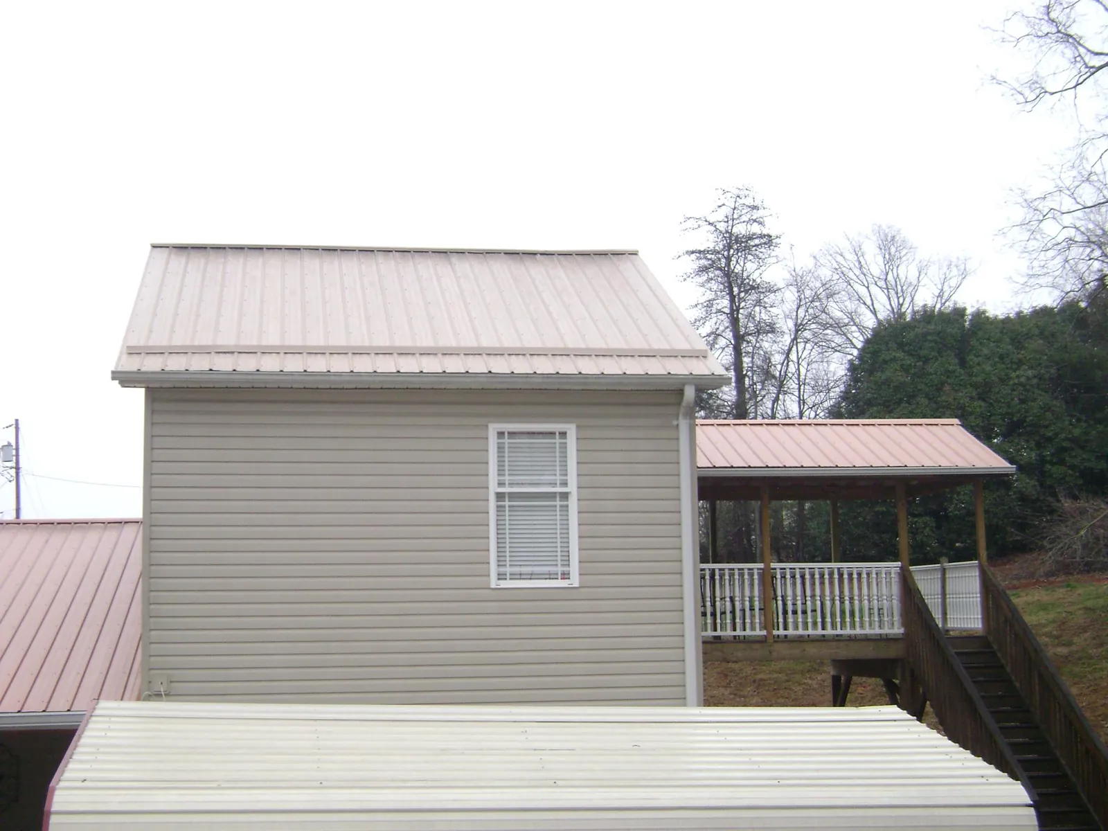 Tan metal roofs on a two story addition and attached porch, from a Roof Replacement job in Cullowhee
