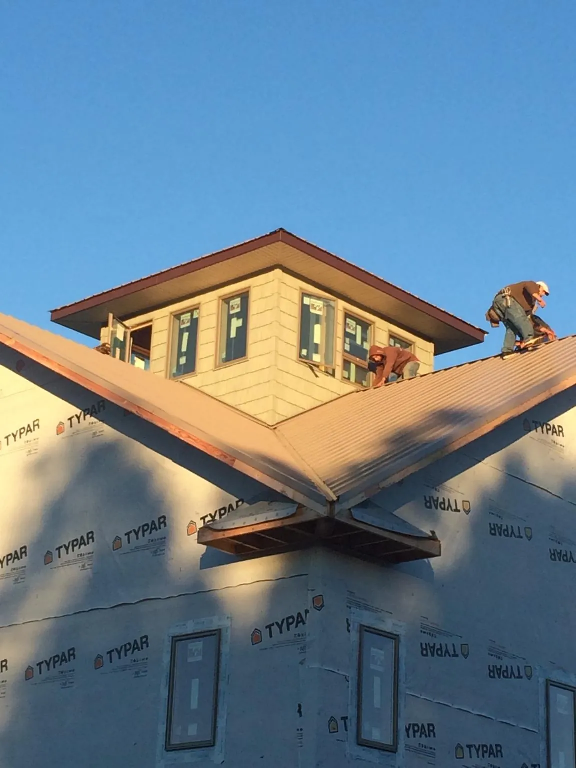 Roofers working around a rooftop cupola on a new metal roof at sunset — Roof Waterproofing in Cullowhee by Roofing Brothers